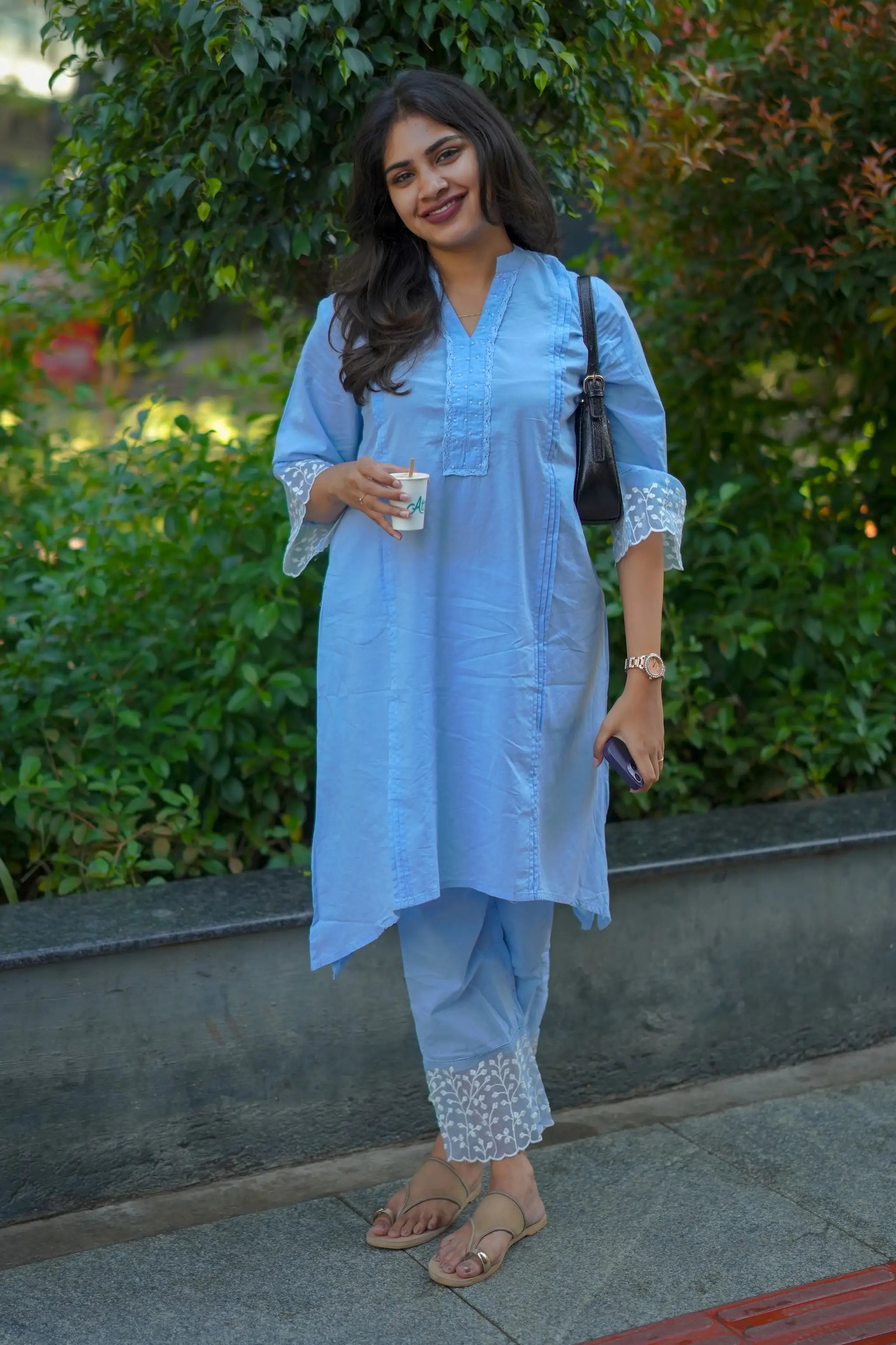 Woman in a light blue outfit standing outdoors with greenery in the background