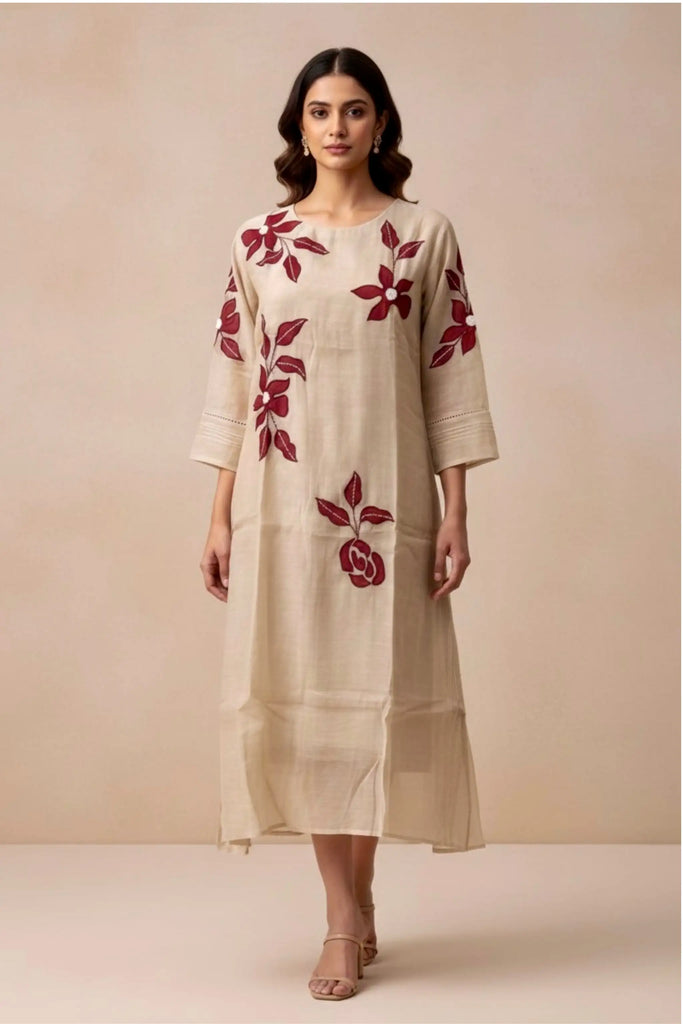 Woman wearing a beige dress with red floral embroidery against a beige background