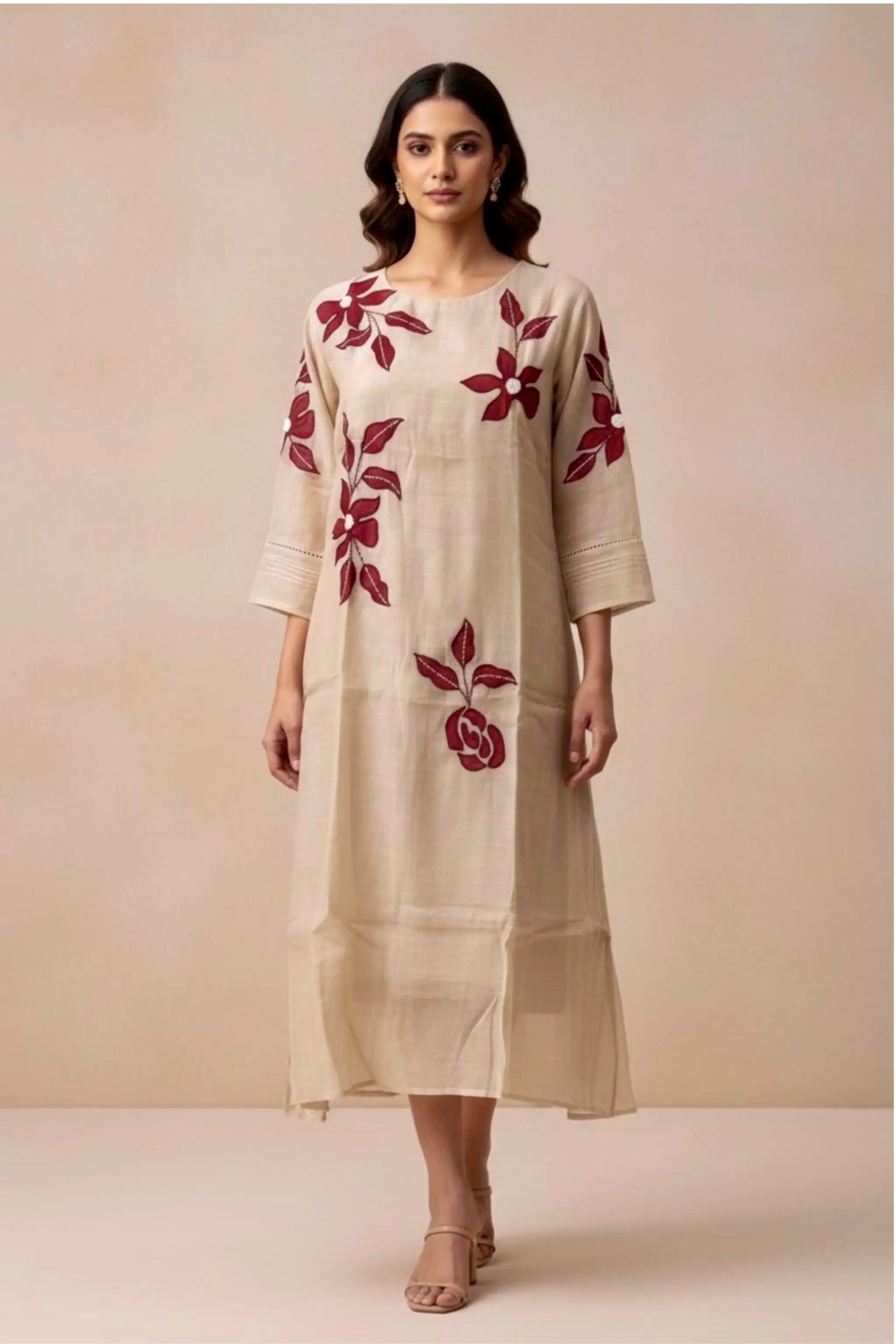 Woman wearing a beige dress with red floral embroidery against a beige background