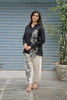 Woman wearing a black embroidered shirt and beige pants standing in front of a blue shutter.