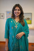 Woman wearing a teal traditional outfit with floral patterns indoors.