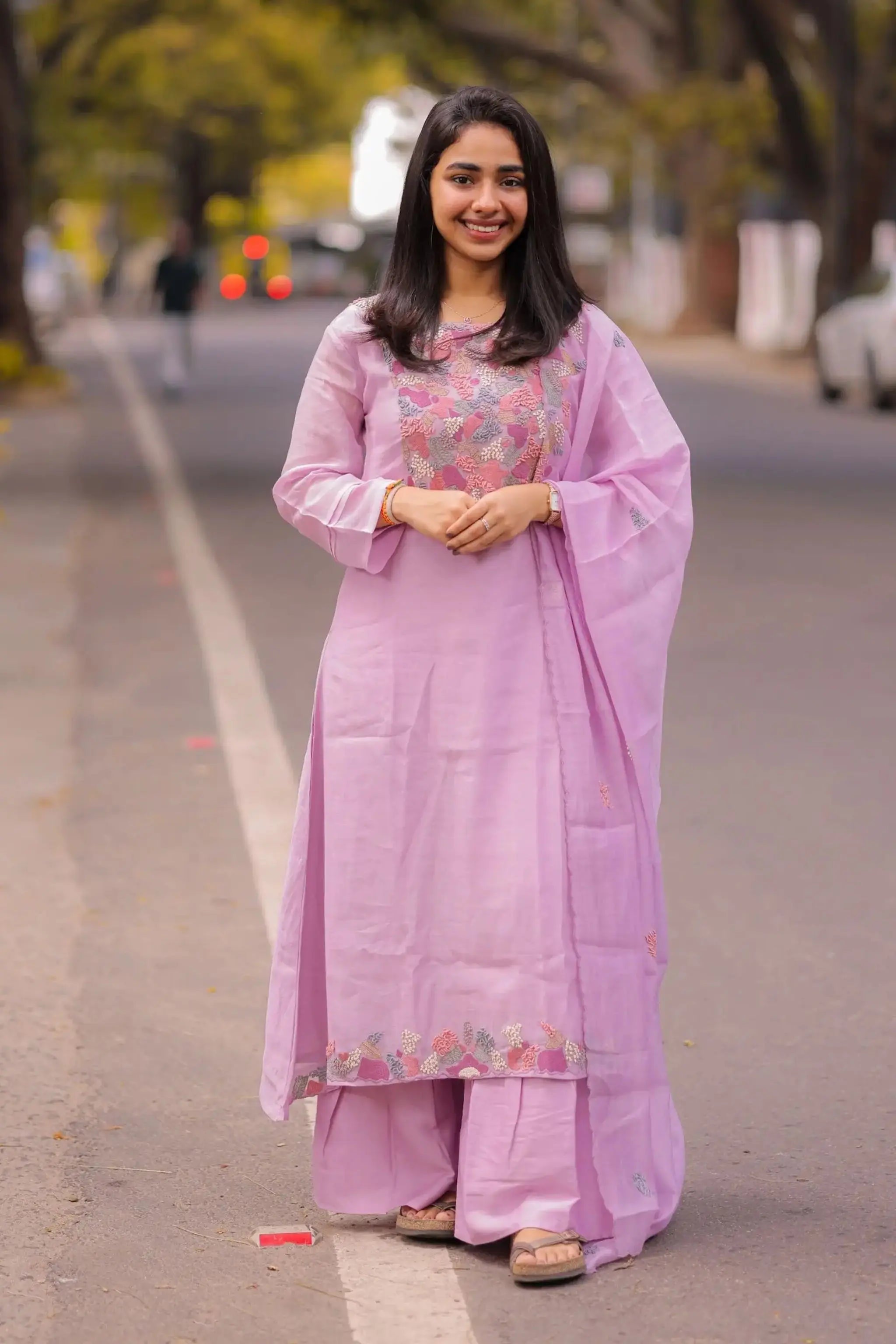 Woman in a pink traditional outfit standing on a road with trees in the background