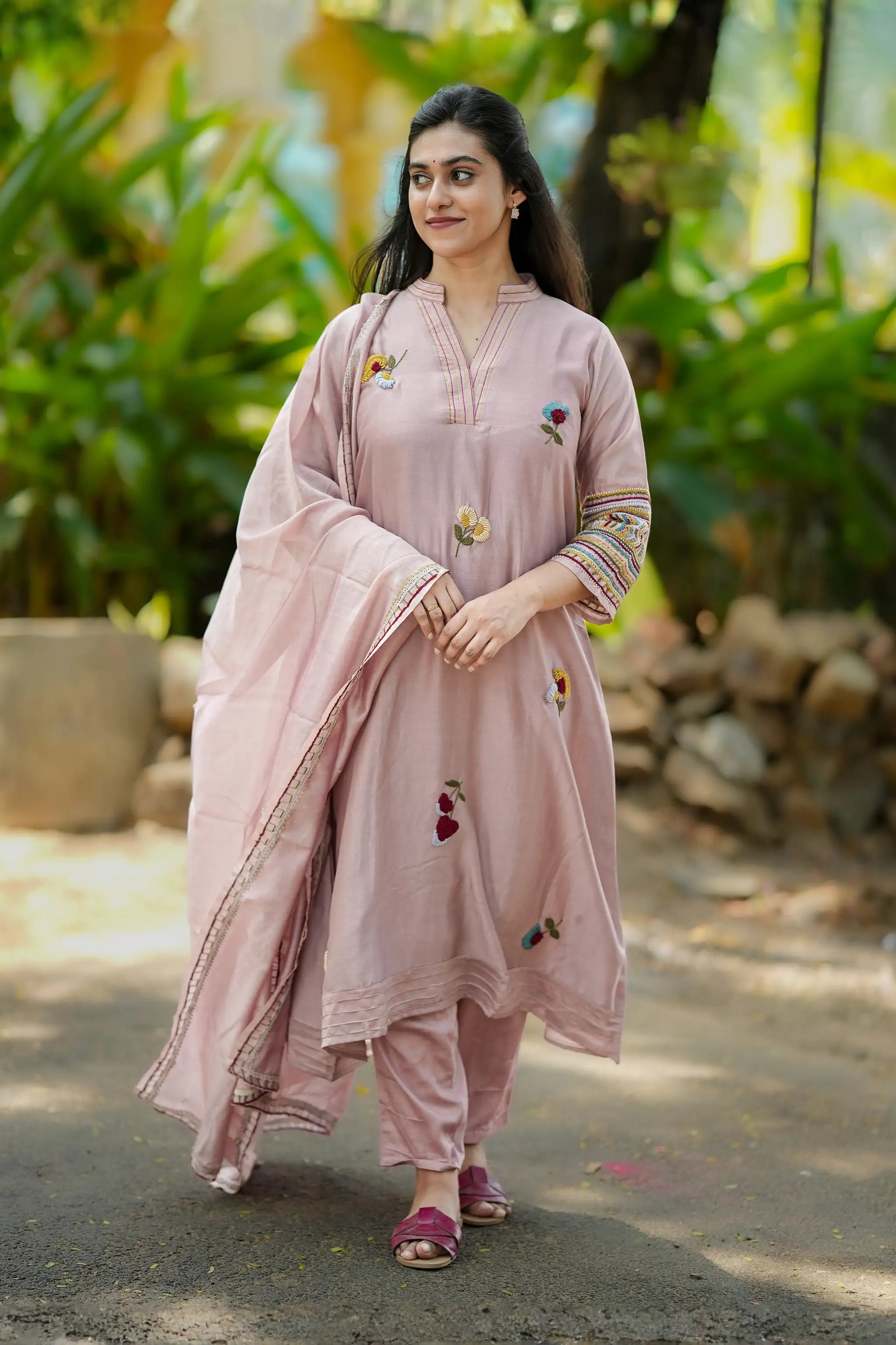 Woman in a pink traditional outfit standing outdoors with greenery in the background