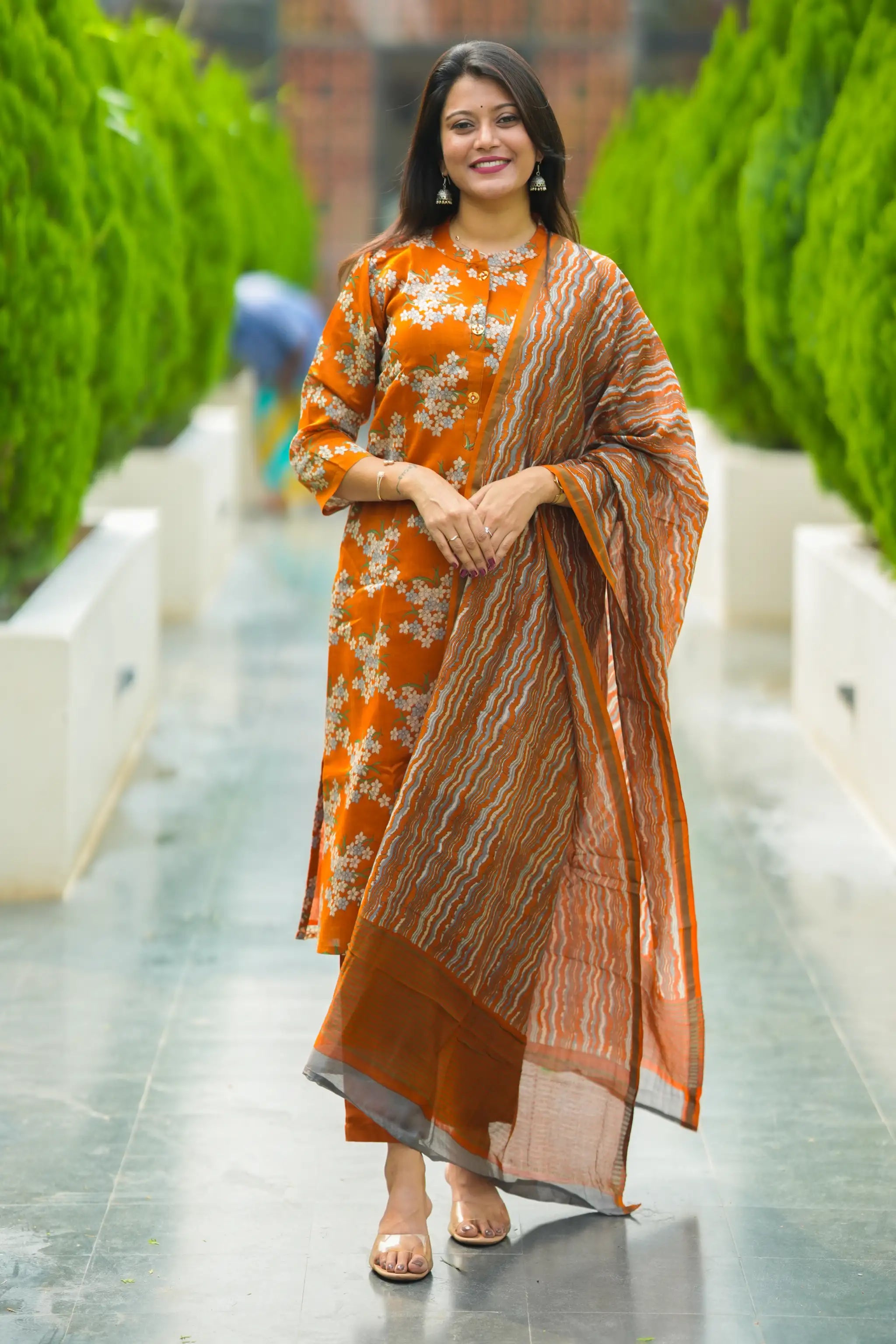 Woman in an orange and white floral dress with a matching shawl standing on a pathway.