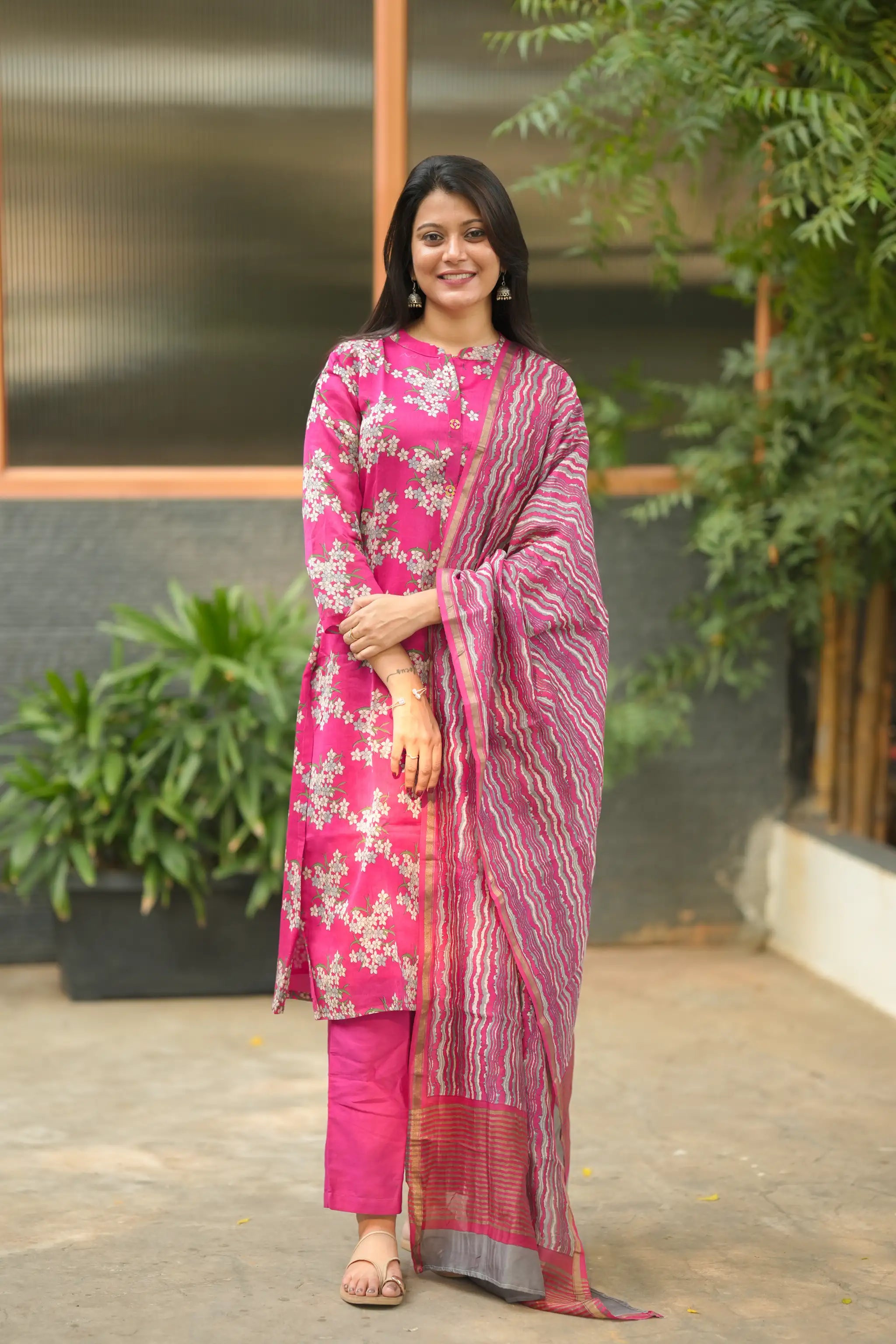 Woman wearing a pink traditional outfit with a patterned dupatta in an outdoor setting.