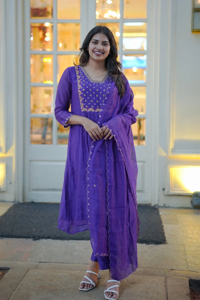 Woman in a purple traditional outfit standing in front of a building entrance.
