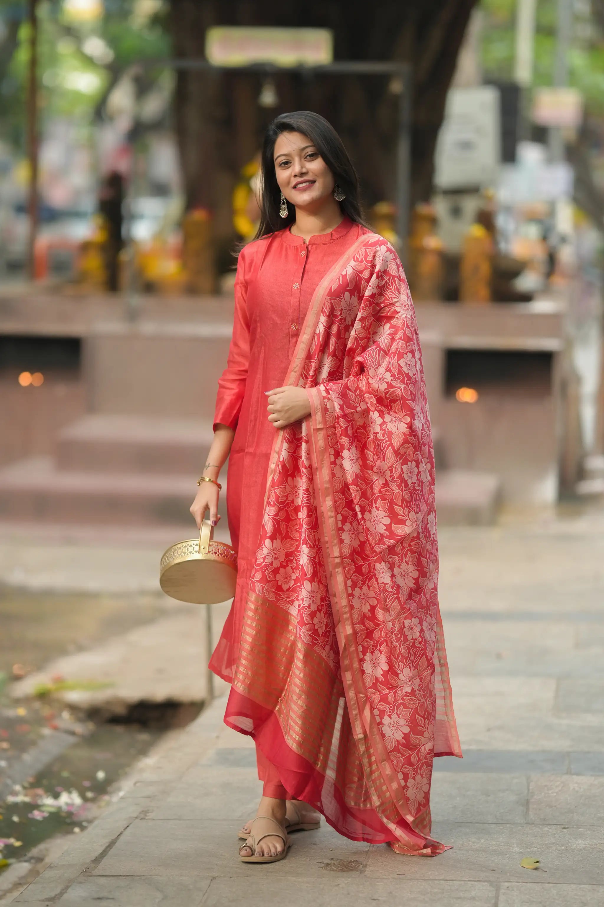 Woman in a red traditional outfit with a floral dupatta standing on a street.