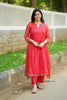 Woman in a red traditional outfit standing outdoors on a path with greenery.
