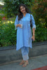 Woman in a light blue outfit standing outdoors with greenery in the background