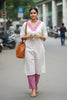 Woman in a white and pink traditional outfit standing on a street.
