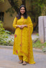 Woman in a yellow traditional outfit standing outdoors with greenery in the background